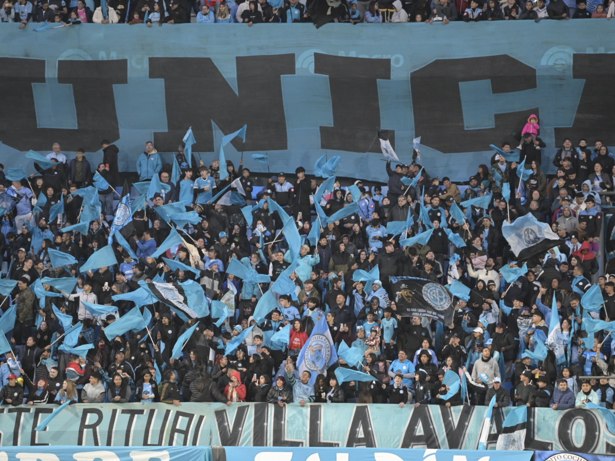 Multitud de hinchas de Belgrano con banderas y camisetas celestes, creando un ambiente de fiesta y apoyo en el estadio