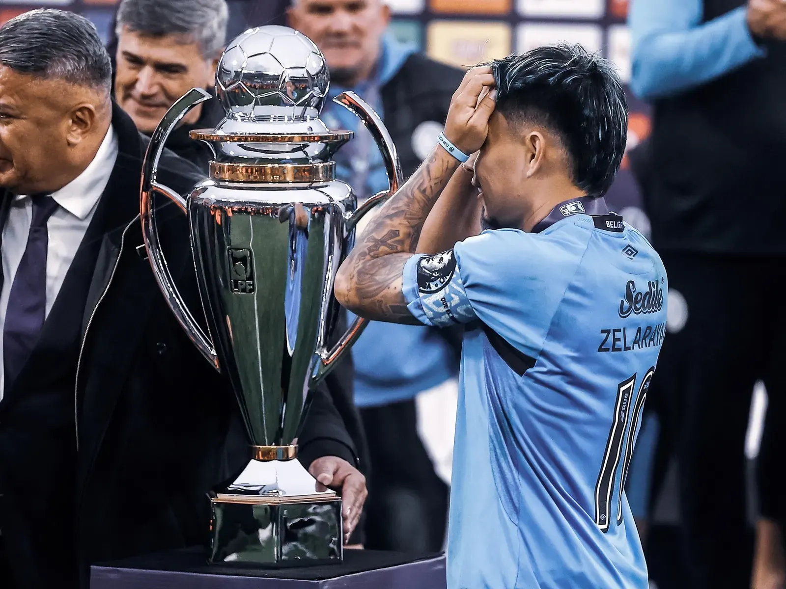 Lucas Zelarayán levanta el trofeo de campeón con Belgrano mientras Ángel Di María lo observa.