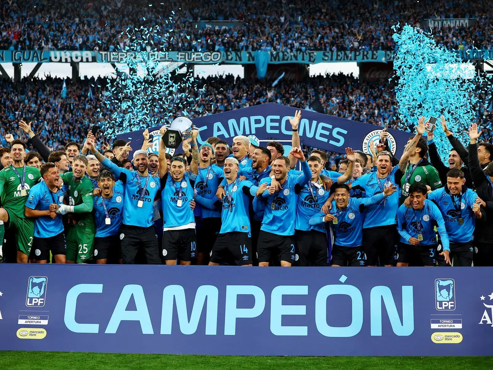 Jugadores de Belgrano celebran en el campo de juego con el trofeo del Torneo Apertura.