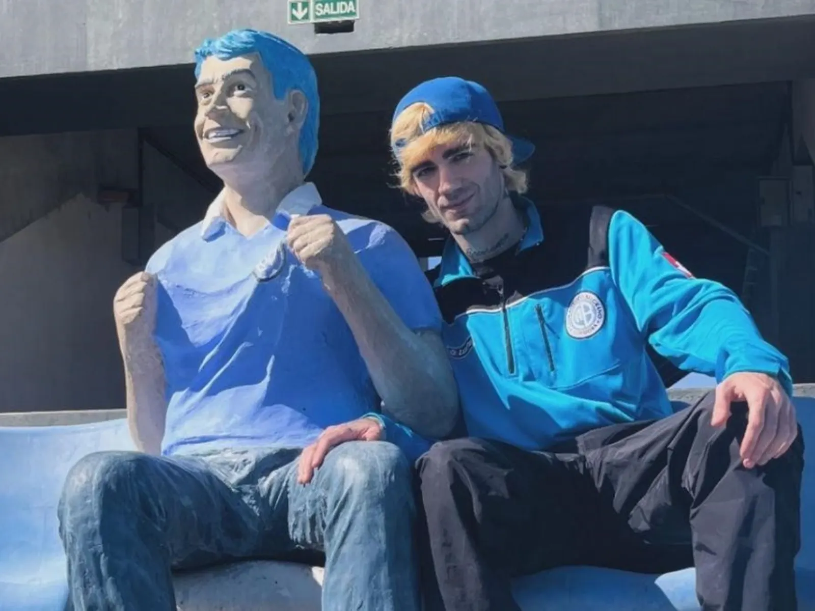 Ramiro Bueno posando con un buzo de Belgrano junto a la estatua de su padre Rodrigo en el estadio de Alberdi.