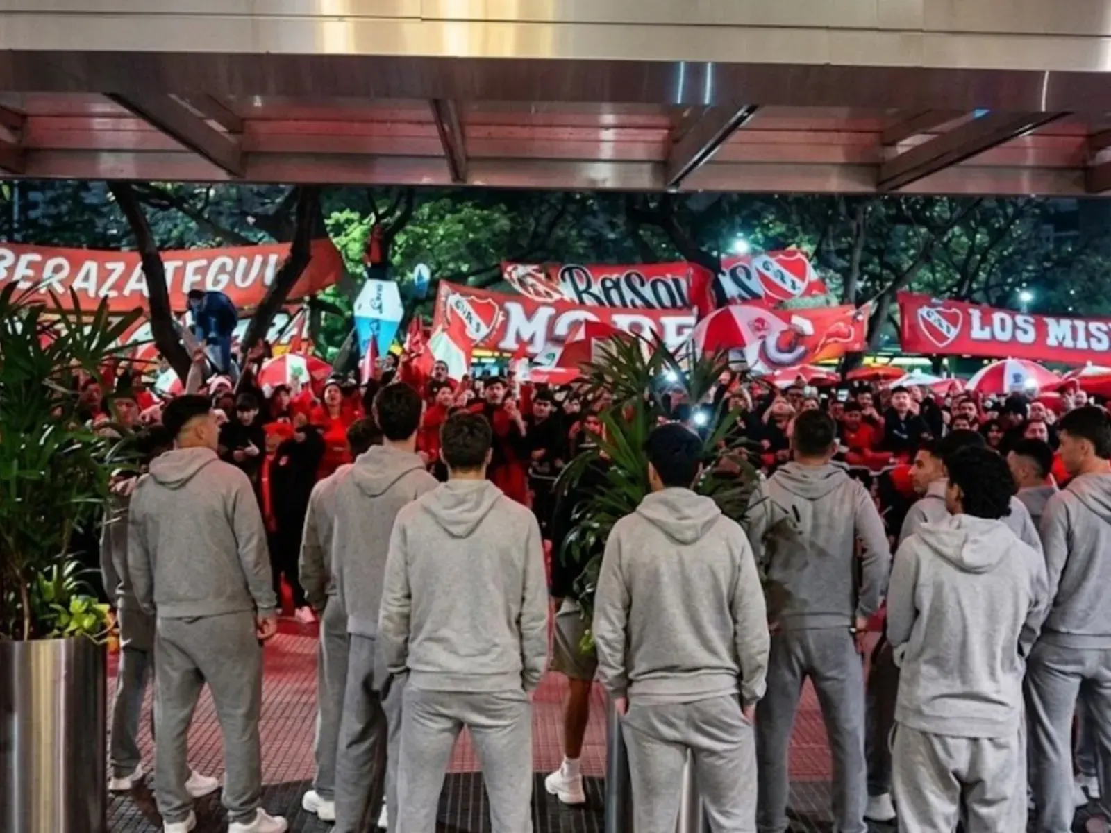Hinchas de Independiente reunidos en la entrada del hotel de concentración con banderas rojas y bombos, en la previa del clásico de Avellaneda contra Racing
